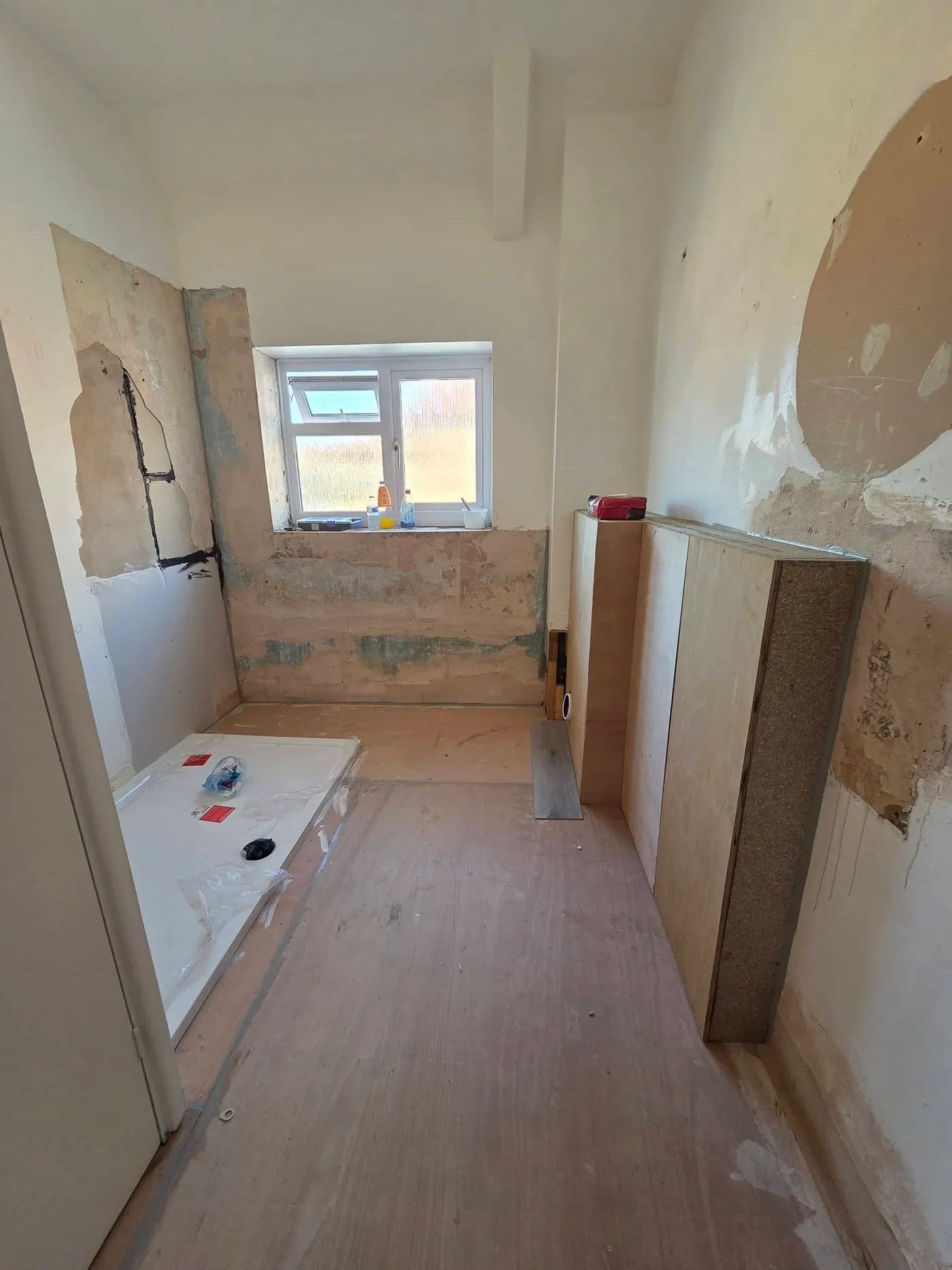 The stripped bathroom with exposed wall surfaces and the shower tray in place.