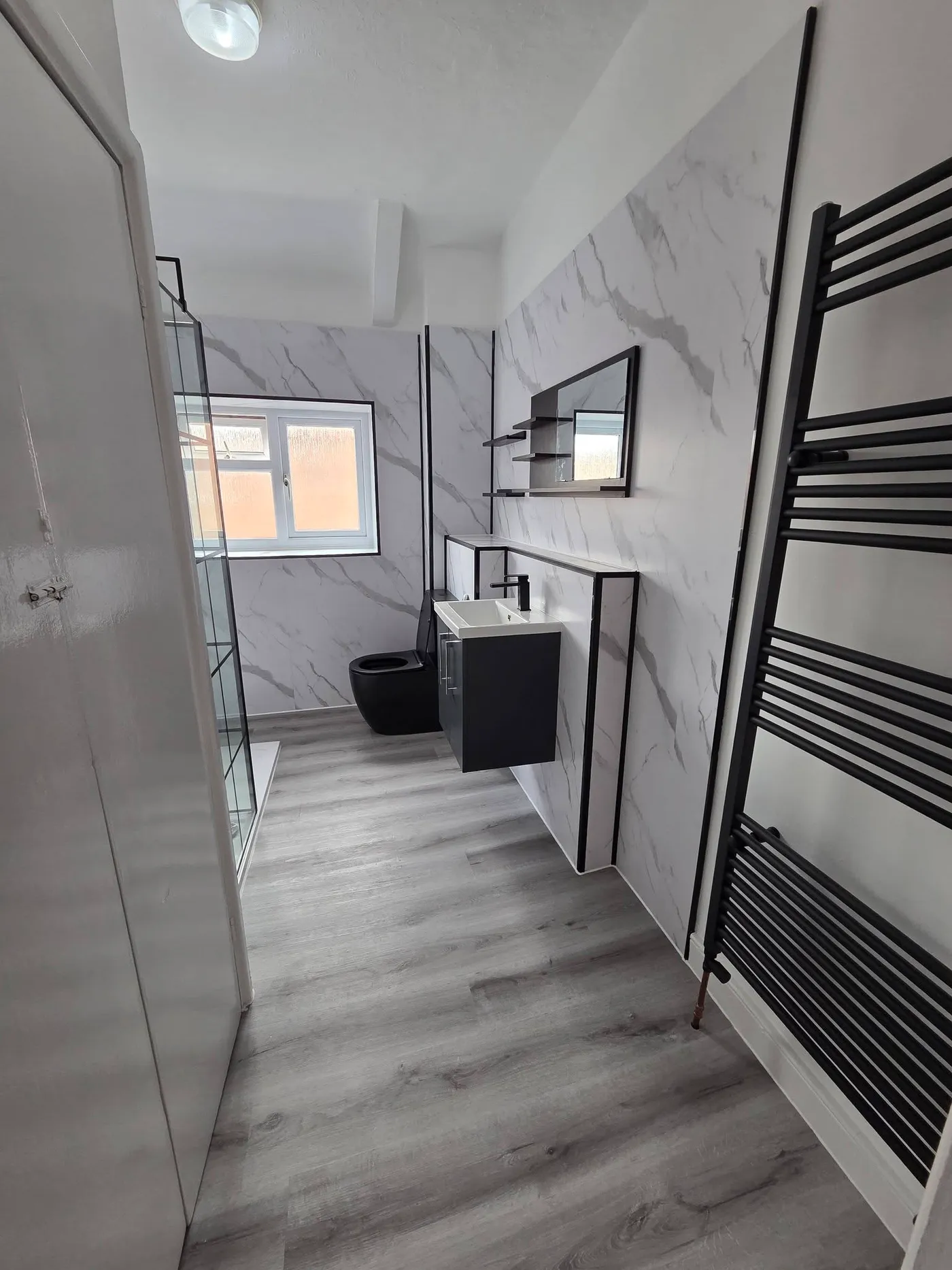 The finished bathroom with marble-effect wall panels, a floating vanity and a black towel radiator.