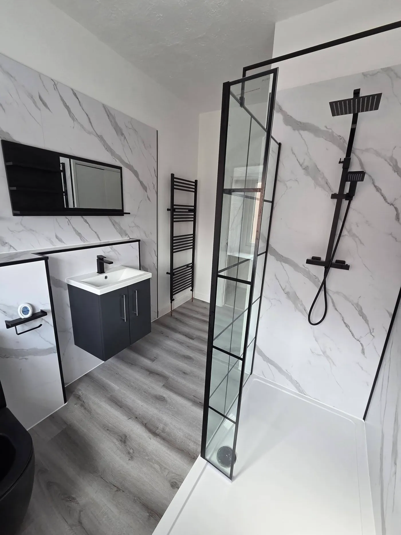 The finished shower screen and wall-hung vanity with grey wood-effect flooring.