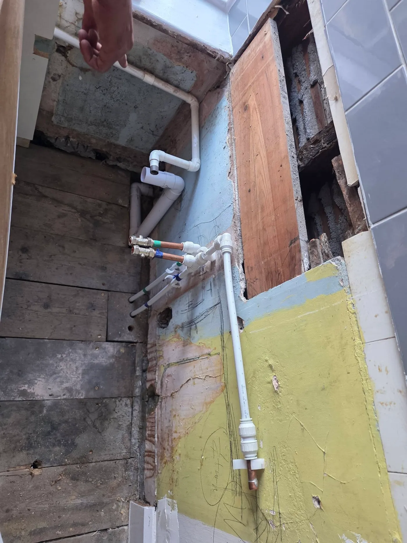 Pipework exposed within the opened bathroom wall.