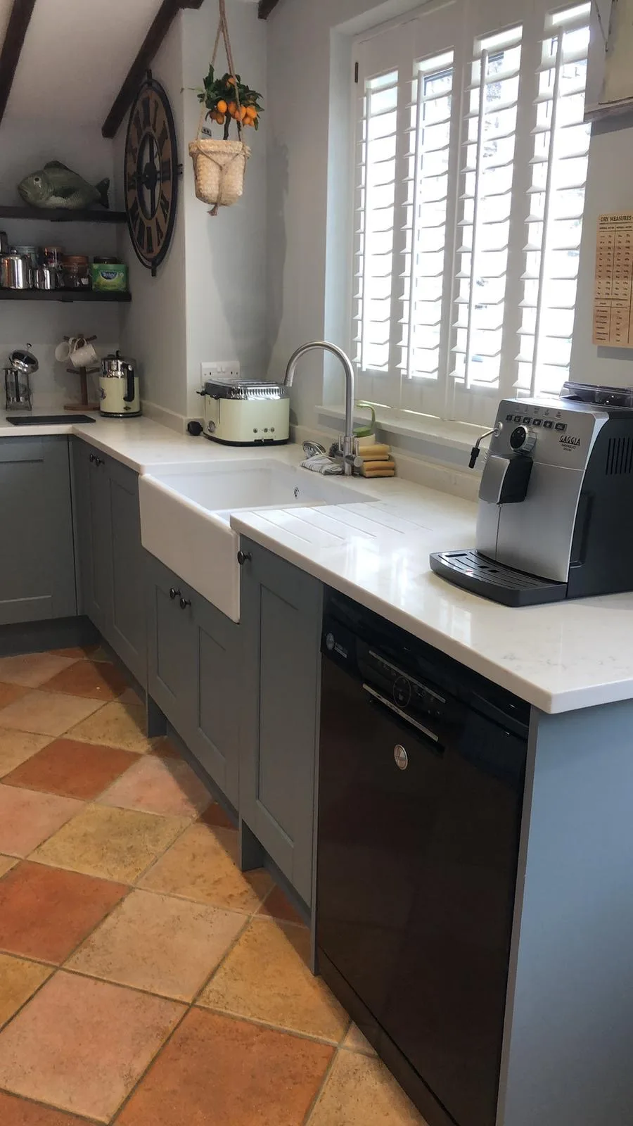 Kitchen run with slate-blue cabinets, a white farmhouse sink, terracotta floor tiles and integrated appliances.